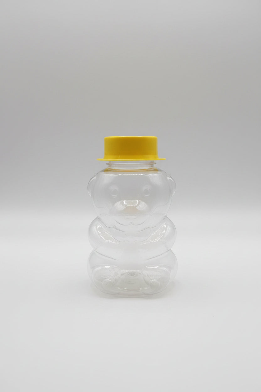 Clear glass bear-shaped container with yellow lid on a cluttered desk
